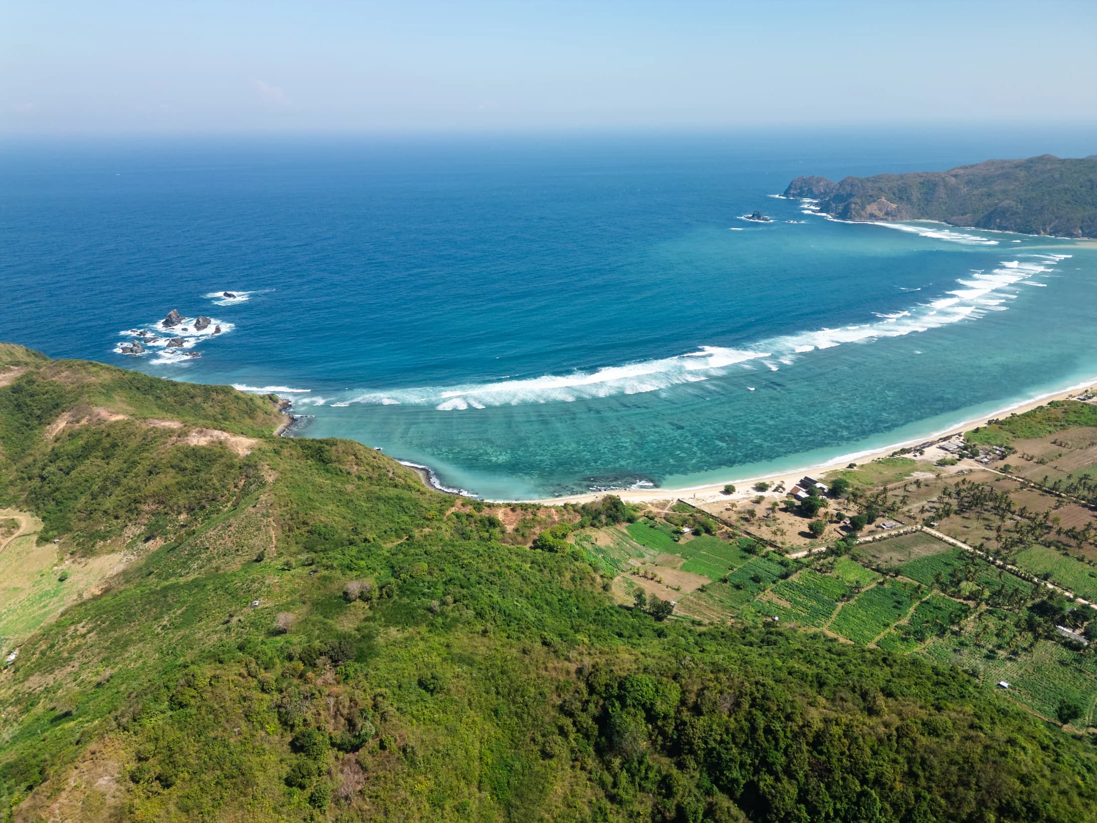 Luchtbeeld van Tampah Bay met turquoise water, een breed zandstrand en groene heuvels in Zuid-Lombok.