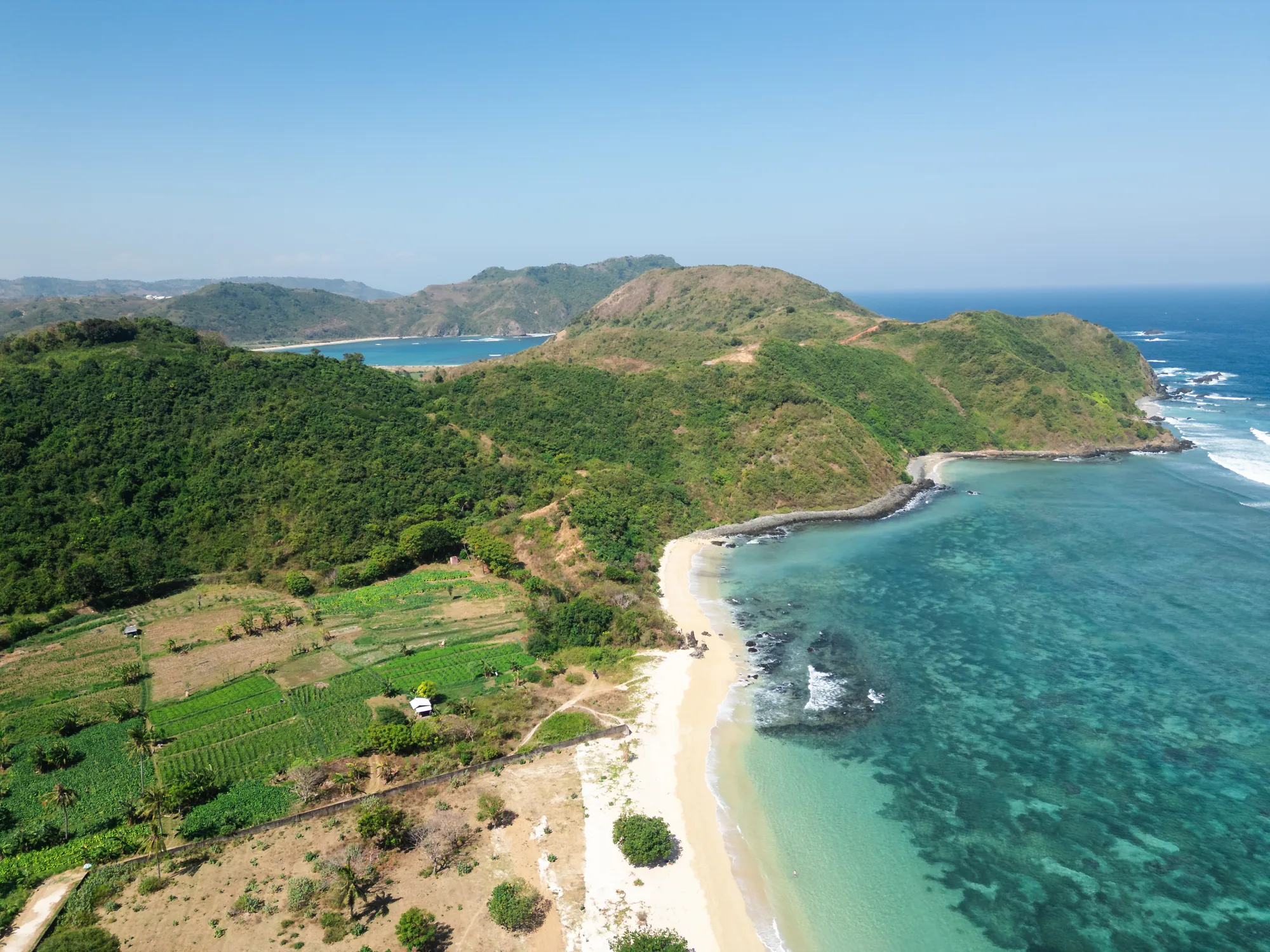 Drone view across Tampah Bay, green coastal hills and clear blue water in South Lombok